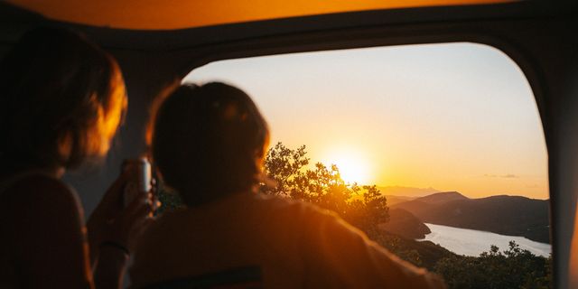 Ein Paar schaut aus ihrem Camper heraus den Sonnenuntergang an