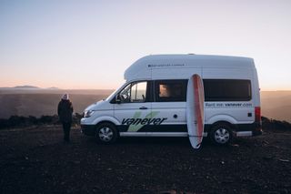 Eine Frau schaut beim Camper den Sonnenuntergang an